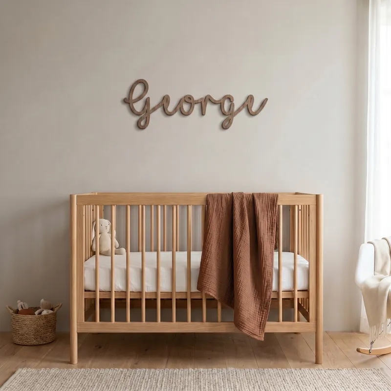 Walnut name sign reading George in the Swirly font, hung above a wooden cot in a nursery